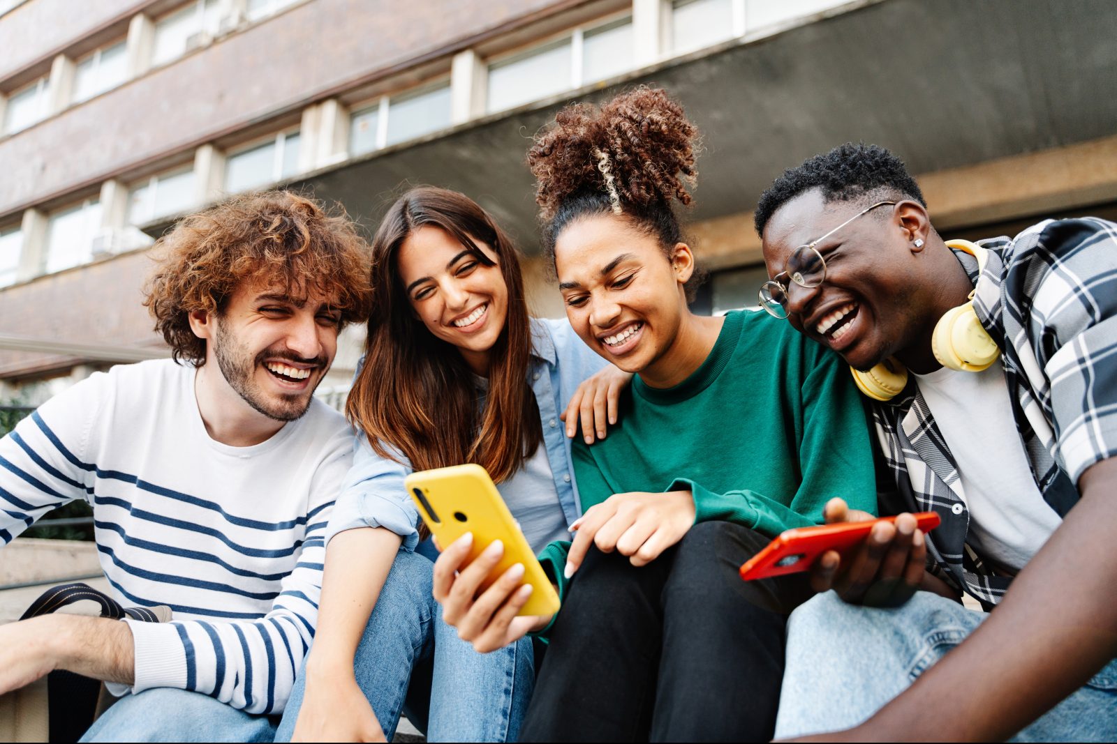 Group of student friends sitting together using mobile phones to share content on social media